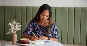 woman at a table journaling while enjoying a cup of coffee.
